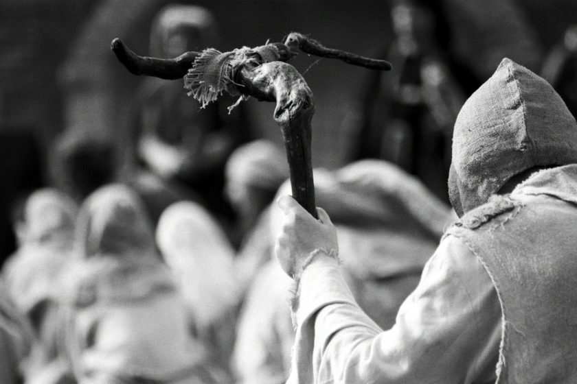 A man seen from the back, dressed like a medieval pilgrim and holding a bifurcated walking stick